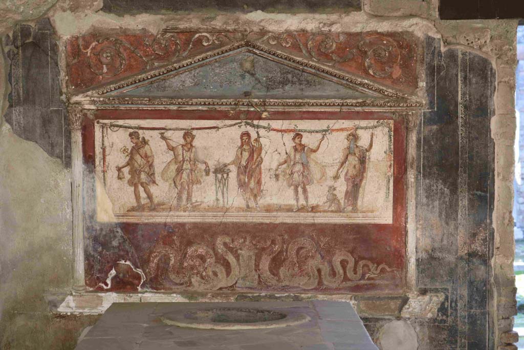 I.8.8 Pompeii. December 2018.Lararium on south wall. Photo courtesy of Aude Durand.
The central figure is the Genius of the household next to a three-legged altar.  
On either side of him are the two Lares. On the left side is Mercury with his money bag.  
On the right side is Bacchus with his panther drinking from a cup held in his right hand.  
Underneath are two serpents approaching a round altar.  
See Fröhlich, T., 1991, Lararien und Fassadenbilder in den Vesuvstädten.  Mainz: von Zabern. (L8: p.252).
