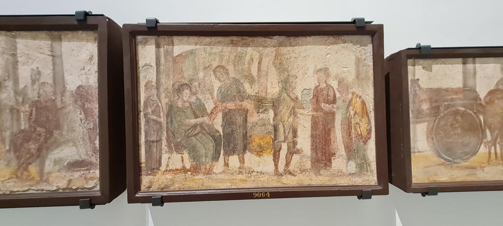 II.4.3 Pompeii. April 2023. Paintings of the Forum frieze, on display in “Campania Romana” gallery in Naples Archaeological Museum.
In centre (inv. 9064) – vendita di tessuti. (Sale of fabrics). Photo courtesy of Giuseppe Ciaramella.
