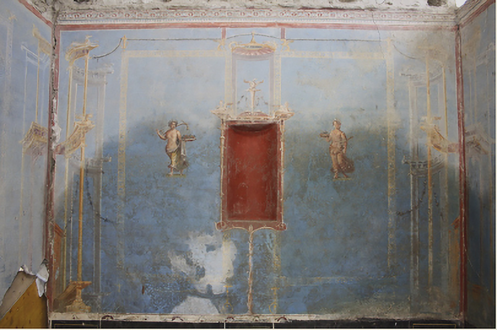 IX.10 Pompeii. House on west side of insula, south of IX.10.1. June 2024. Sacrarium room 32 south wall with blue decoration, showing niche in red with figures either side.
On the left is an allegorical agricultural image with a female figure carrying a form of plough on her shoulder and a tray with first fruits in her hand.
On the right is an allegorical agricultural image with a female figure holding out a basket of first fruits and with a curved stick under her arm.
See PAP 15-E-Journal-Sacrario-Regio-IX.pdf, fig. 14, p. 9, and detailed photos of the two figures, fig. 18, fig. 19, p. 11.
Photograph © Parco Archeologico di Pompei.

