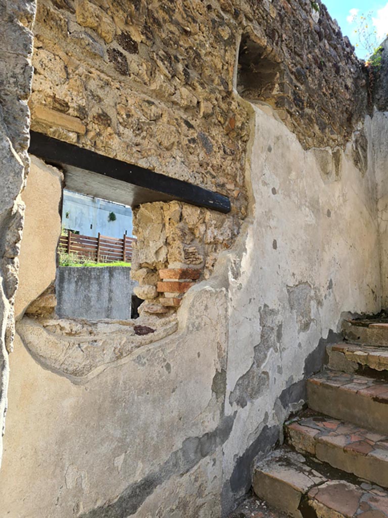 Villa of Diomedes, Pompeii. May 2024. 
East wall at side of stairs, with lararium niche in upper wall with window below. Photo courtesy of Klaus Heese.
According to Boyce,
Just to the right of the main entrance six steps lead down to the servants’ quarters, and in the wall beside this stair is a piccolo larario – apparently only a niche, in which a statuette of Minerva was found.
See Boyce G. K., 1937. Corpus of the Lararia of Pompeii. Rome: MAAR 14, (p.97, no.476).
See Giacobello, F., 2008. Larari Pompeiani: Iconografia e culto dei Lari in ambito domestico. Milano: LED Edizioni, (p.221, no.3)
