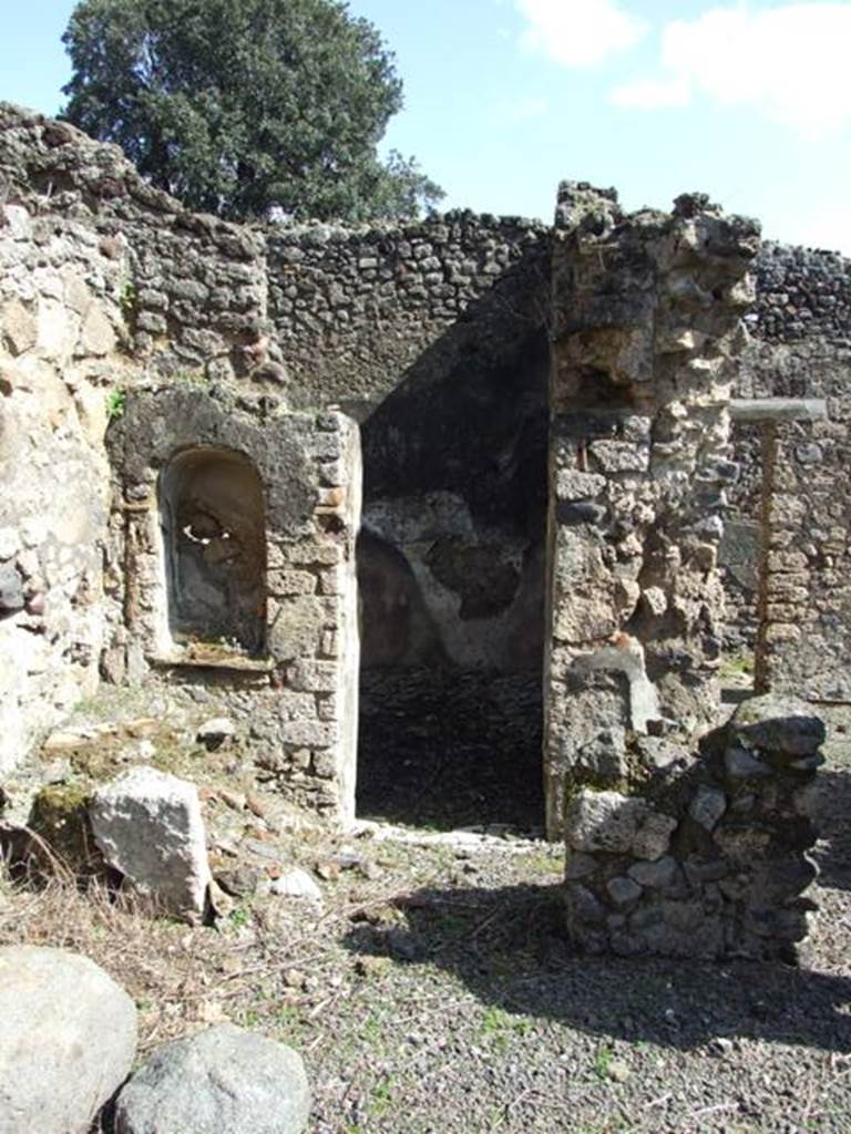 V.4.9 Pompeii. March 2009. Kitchen on east side of atrium. Looking east. According to Boyce, on the south-east corner of the impluvium was a square column (see remains on right of photo). This column closed off part of the east side of the impluvium to provide a small area as a kitchen. In the west side of this column, facing the impluvium, was a niche with slightly arched ceiling and projecting floor. Above and to the right of the niche was a yellow laurel wreath with pendent taeniae hung from a nail – all in stucco relief (see photo below). Within the niche were found – an iron knife with bronze handle, an iron hammer, and a bronze rosette. On the same side of the column, but higher, was another larger rectangular niche, probably for storage purposes.
See Boyce G. K., 1937. Corpus of the Lararia of Pompeii. Rome: MAAR 14. (p.41, no.124, Pl.4,5) 
Hardly anything remains of the column today, and neither niche.

In the north-east corner of the kitchen stood a small hearth and above it in the east wall was a high arched niche (see above photo, on the left). Its walls were coated with white stucco. On its floor stood a masonry block, apparently for use as an altar, behind it a step was built against the rear wall. In the centre of the step was a mark left by an oval object which had stood there, probably a statuette. Another altar, terracotta and cylindrical, was found within the niche.
See Boyce G. K., 1937. Corpus of the Lararia of Pompeii. Rome: MAAR 14. (p.41, no.125, Pl.4,5) 
