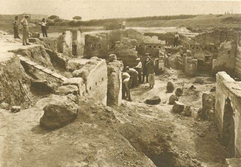 I.9.13-14 Pompeii. 1952 photo taken during excavation. Looking south through tablinum 6 to entrance at I.9.13. This photo shows the excavations in progress and the “ground level” is still several feet above the level today. Only the top half of the tablinum wall on the right has been uncovered. The missing plaster in the centre and the plaster decoration on the wall matches that in the photo of the now enclosed tablinum above. The matting on top of the wall is also in the 1952 picture of room 7 which is behind this wall. A tapered window in room 15 can also be seen in the far right of the photograph. In the Illustrated London News this was published as being a recent excavation on the north side of the Via dell’Abbondanza. I.9.13-14 has its main entrance at I.9.13 on the north side of Via di Castricio, but south of Via dell’Abbondanza. Photo courtesy of Rick Bauer.