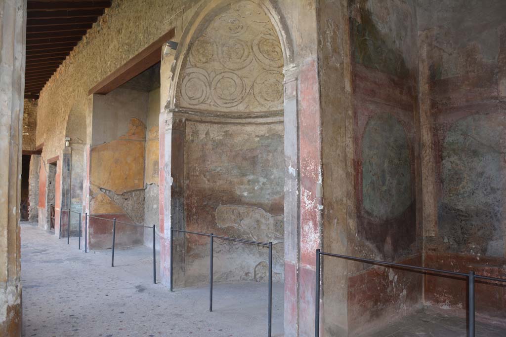 I.10.4 Pompeii. September 2019. Looking towards south side of south portico, from south-west corner.
On the right is Alcove 25 (Sacrarium), followed by Alcove 24, 23, and 22 and doorway to 21, in south-east corner.
Alcove 24 has a domed top decorated with stucco, underneath which is a painting of Venus and cherubs in a temple.
Alcove 23 has the painting of the seated poet Menander. 
Alcove 22 also has a domed top decorated with stucco, underneath which is a painting of Diana and Acteon.
Room 21 has a mosaic emblema of satyr and maenad in the centre of the mosaic floor.
Foto Annette Haug, ERC Grant 681269 DCOR.

