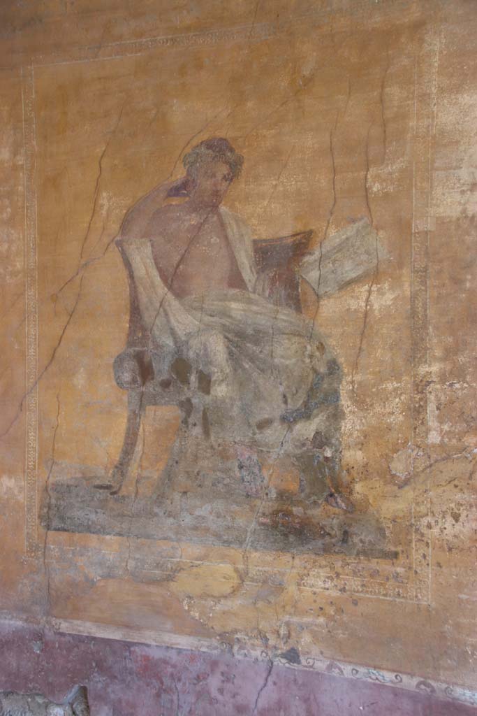 I.10.4 Pompeii. September 2021. 
Alcove 23, west wall with wall painting of a seated poet. Photo courtesy of Klaus Heese.
The name of Menander was inscribed by the painter on the skirt of the mans cloak. 
In this alcove there are also painted masks, with possibly Bacchus sitting on a chair with a robe covering his legs, and a painted table.

