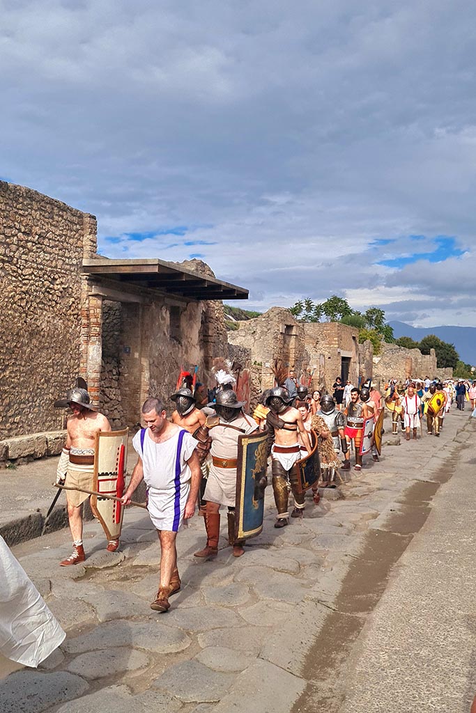 III.5.2 Pompeii, on left. 28th September 2024. 
Gladiators on their way to the Forum from the Amphitheatre, during “Ludi Pompeiani” event.
Looking east along north side of Via dell’Abbondanza. Photo courtesy of Giuseppe Ciaramella.
