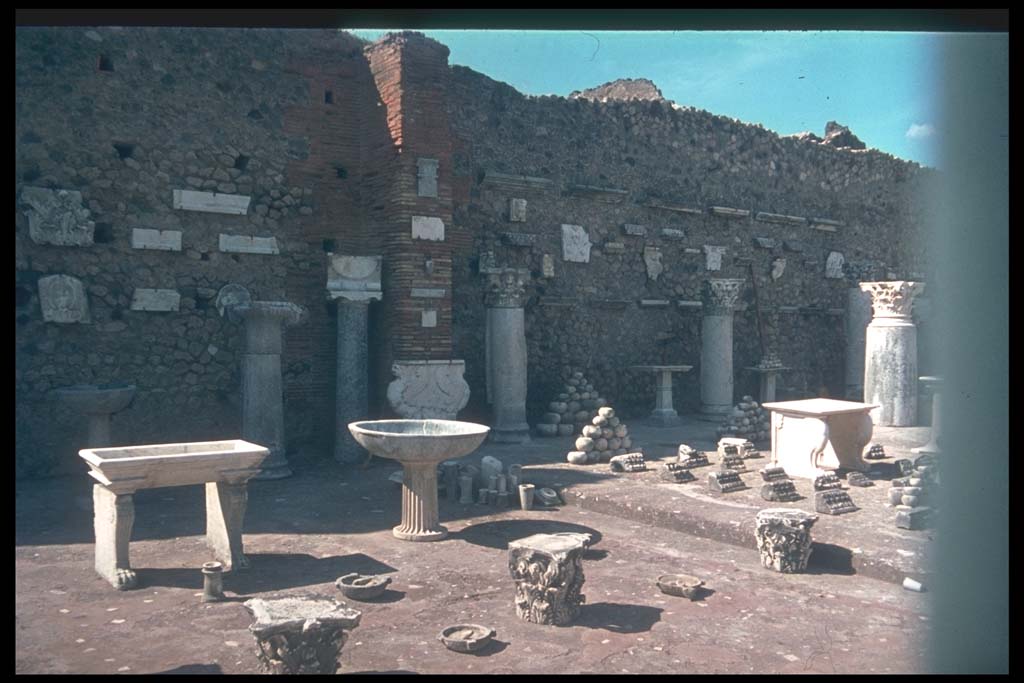 VII.7.29 Pompeii. Items on display and in storage. Photographed 1970-79 by Günther Einhorn, picture courtesy of his son Ralf Einhorn.
According to Garcia y Garcia, it was Maiuri that restored the pilasters of this building and formed it into a display area. Mostly these items on display are clay amphorae and domestic items from the houses, shops and workshops. For the most part without provenance and classified only by type and form. The bombing of 13th September 1943 caused the demolition of the south and part of the west wall, and at least two of the seven pilasters of the entrance doorways. In 1946 Maiuri again restored the pilasters and roof.
See Garcia y Garcia, L., 2006. Danni di guerra a Pompei. Rome: L’Erma di Bretschneider. (p.116-7)

