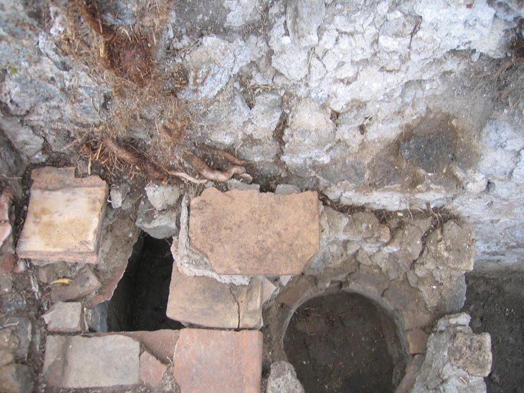 VIII.7.10 Pompeii. August 2005. Looking down onto hearth against south wall in kitchen.
The remains of the niche of the lararium may be still partially visible in the wall above the hearth, upper centre of photo.
Photo courtesy of Pompeii Archaeological Research Project: Porta Stabia.
Site of kitchen, described by Eschebach as having hearth, well and lararium.
See Eschebach, L., 1993. Gebäudeverzeichnis und Stadtplan der antiken Stadt Pompeji. Köln: Böhlau. (p. 389)
According to Boyce, in the wall of the kitchen there was a niche and beside it was a lararium painting.
It represented a sacrificial scene with the Genius and the tibicen, one on each side of an altar.
On either side of them was a Lar. In the lower zone was a single serpent beside an altar.
See Boyce G. K., 1937. Corpus of the Lararia of Pompeii. Rome: MAAR 14. (p.78, no.377).
See Sogliano, A., 1879. Le pitture murali campane scoverte negli anni 1867-79. Napoli: (p.12, no.24, “badly preserved”).
According to Mau  -
“Next to the hearth there was the usual painting of the Lares, and a niche.”
See Mau in BdI, 1875, (p.166 - La quarta casa). 


