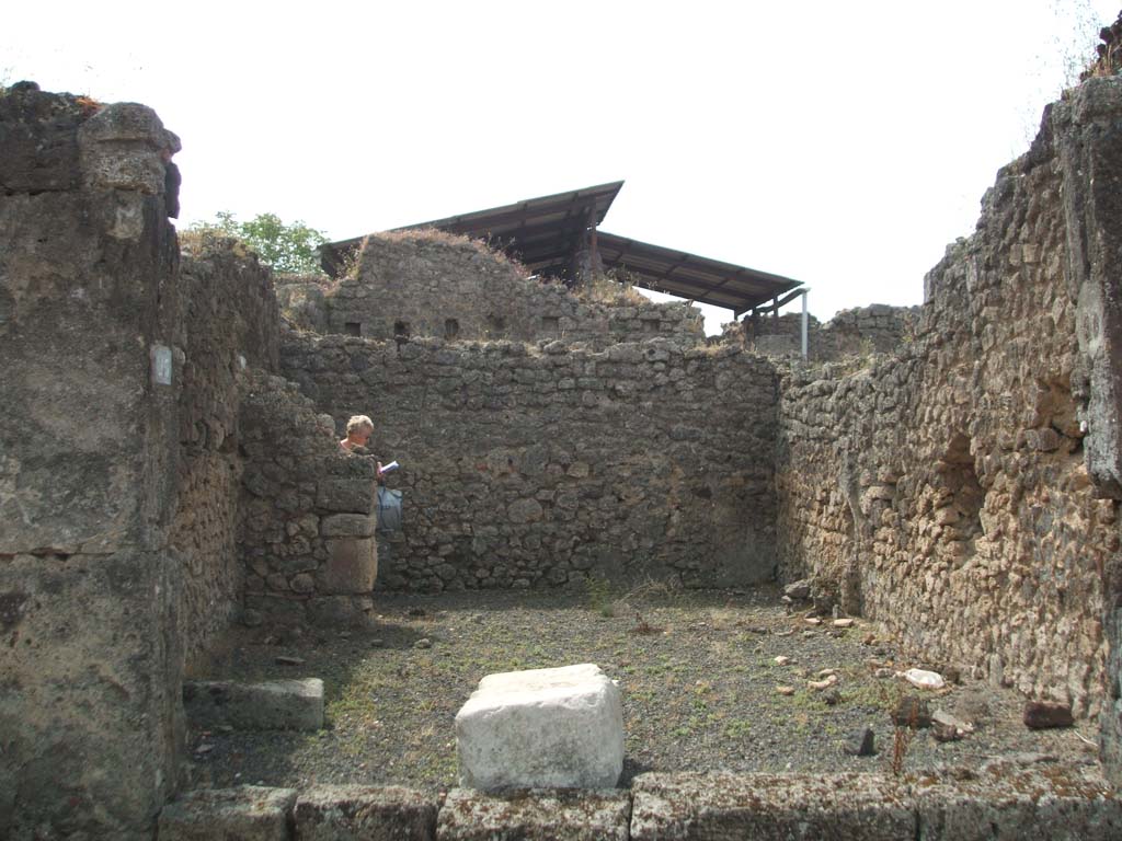 IX.7.23 Pompeii. May 2005. Looking south across caupona to narrow rear room.
According to Mau, immediately behind the threshold of the main room, lay a large stone square block of travertine (0.90 long, 0.58 wide and 0.46 high).
He thought this probably served as the base for a wooden table, around which the customers would settle down to eat.
He also said the threshold of this main room seemed to have been made of wood.
See Mau in Bullettino dell’Instituto di Corrispondenza Archeologica (DAIR), 1882 (p.183)
According to Eschebach, the podium used to be on the west side (right of photo) of the caupona, the rear room had the hearth and a window looking into the caupona.
See Eschebach, L., 1993. Gebäudeverzeichnis und Stadtplan der antiken Stadt Pompeji. Köln: Böhlau. (p.435)

According to Della Corte, this caupona was attributed to Ti. Claudio Epafrodito, because of the seal/signet brought to light here –
Ti. C(laudius) Ep(aphroditus)    [CIL X 8058,9]. 
He was well noted as producer of wine, one of his numerous named amphora was found in an adjacent atrium. 
See Della Corte, M., 1965. Case ed Abitanti di Pompei. Napoli: Fausto Fiorentino. (S.27 on p.197)

