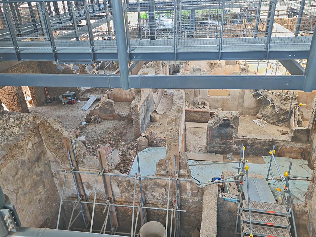 IX.12.4 Pompeii. June 2024. Looking west from above bakery in room “f” of IX.12.6. Photo courtesy of Giuseppe Ciaramella.
The atrium “c” of IX.12.4 is on the left. 
On the north side of the atrium are rooms “e” and “f”. Room “f” is at the rear (west) side of the oven, (centre left of above photo).

