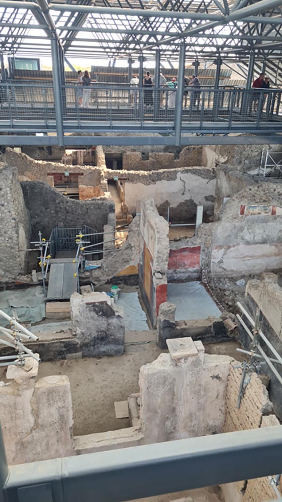 IX.12.4/6 Pompeii. June 2024. 
Looking east from above IX.12.4. Photo courtesy of Giuseppe Ciaramella.
Looking east towards room “o”, with modern steps down into IX.12.6, and yellow and black painted walls.
Room “l(L)” with red walls is on its south side.
On the right is room “f”, with painting on upper wall, described as a painted zoccolo.

