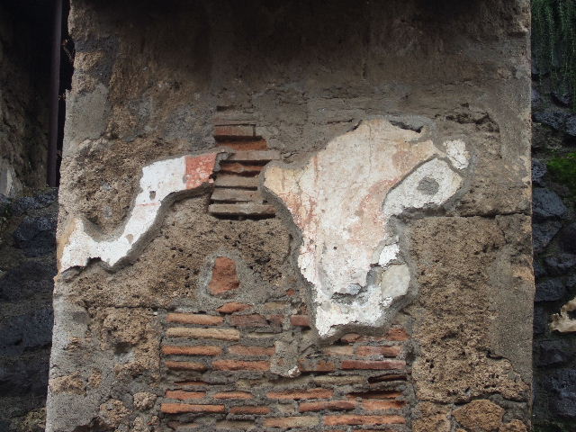 IX.13.5 Pompeii. May 2005. Remains of painted plaster between IX.13.4 and IX.13.5. Visible on the left of the plaster is one red square of the checkerboard pattern that covered the façade. Visible on the right of the plaster are the remains of the figure of Romulus, head, shoulder and cloak.
