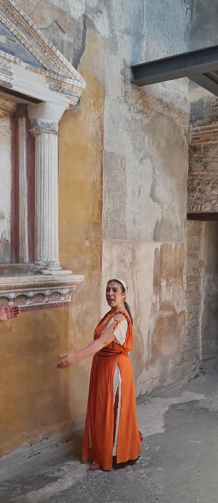 VI.15.1 Pompeii. 8th June 2024. 
Actress playing part of slave in front of household lararium.
Photo courtesy of Giuseppe Ciaramella. 
Historical reconstruction entitled L’altra Pompei prende vita (The other Pompeii comes to life).
